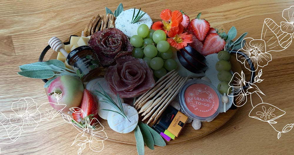 Charcuterie board with artfully arranged meats, cheeses, fresh and dried fruits, nuts, olives, pickles, crackers, jams, honey, and a sweet- on a wood board.