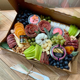 Charcuterie meats, cheeses, fruit, nuts, olives, pickles and accompaniments on a tray inside a Kraft box. Serves 6-8 as appetizer portions. The Gathering.