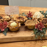 Assorted mini pies on a wooden board with decorative flowers and a card in the background.